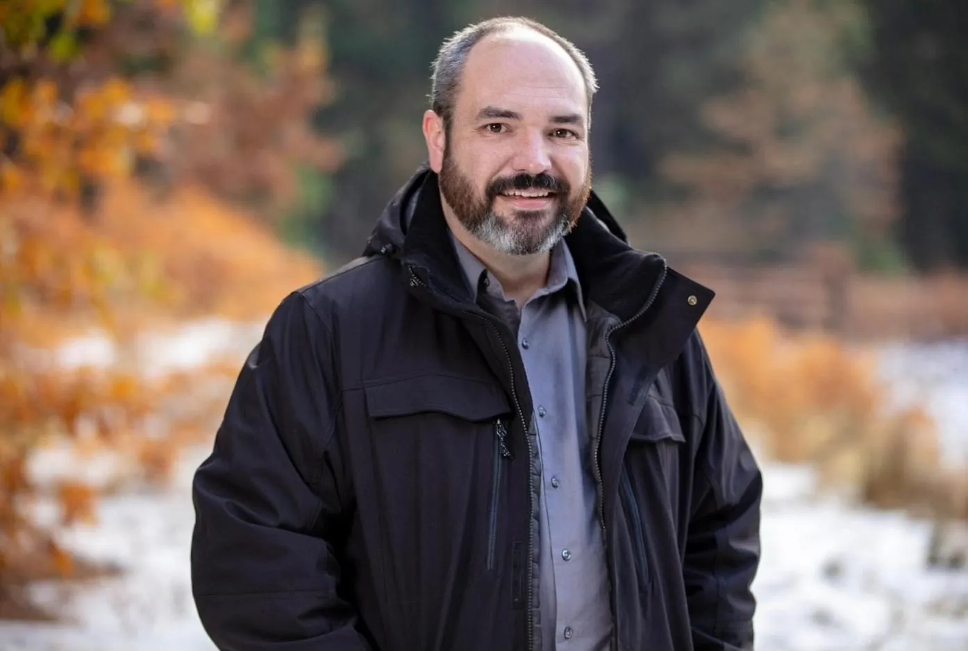 Allan Claghorn in a dark jacket in an autumn forest with early snow.