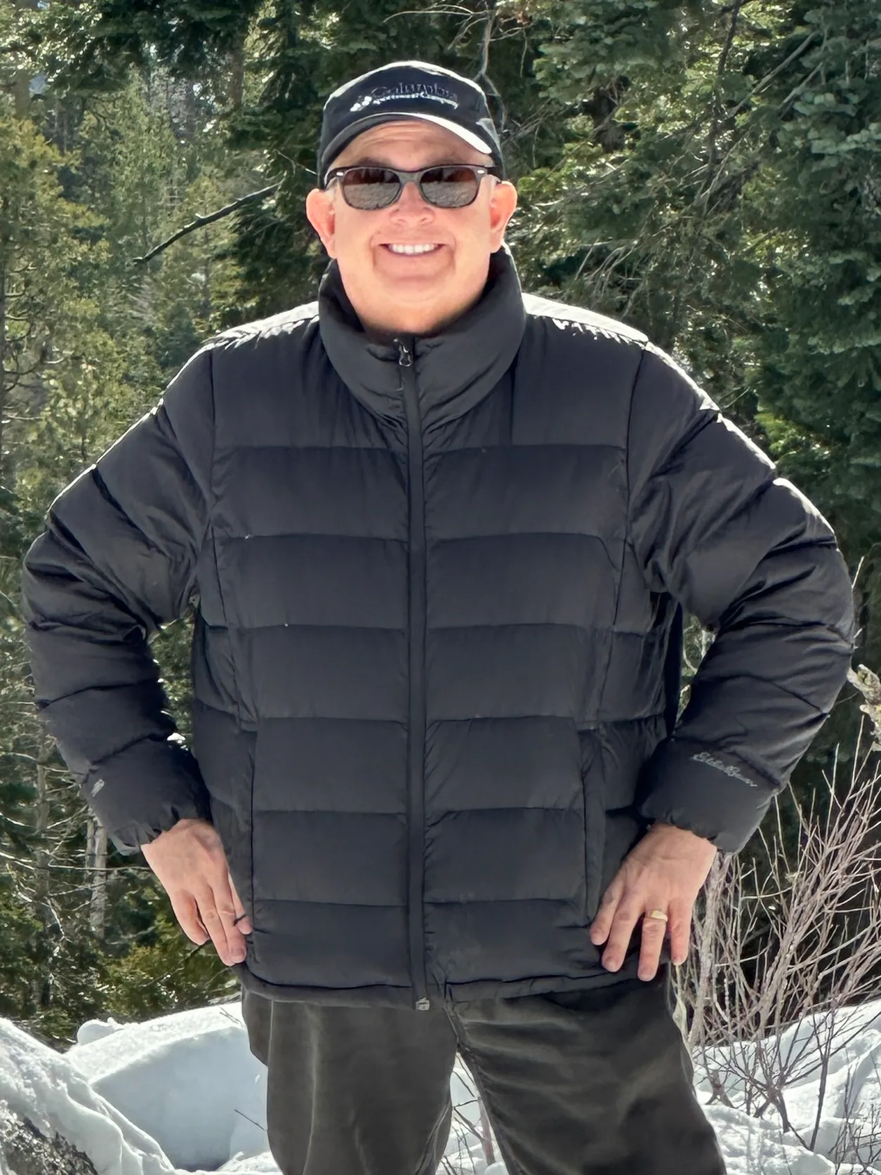 Jay Goldberg smiling in a black winter jacket and cap in a snowy Sierra forest.